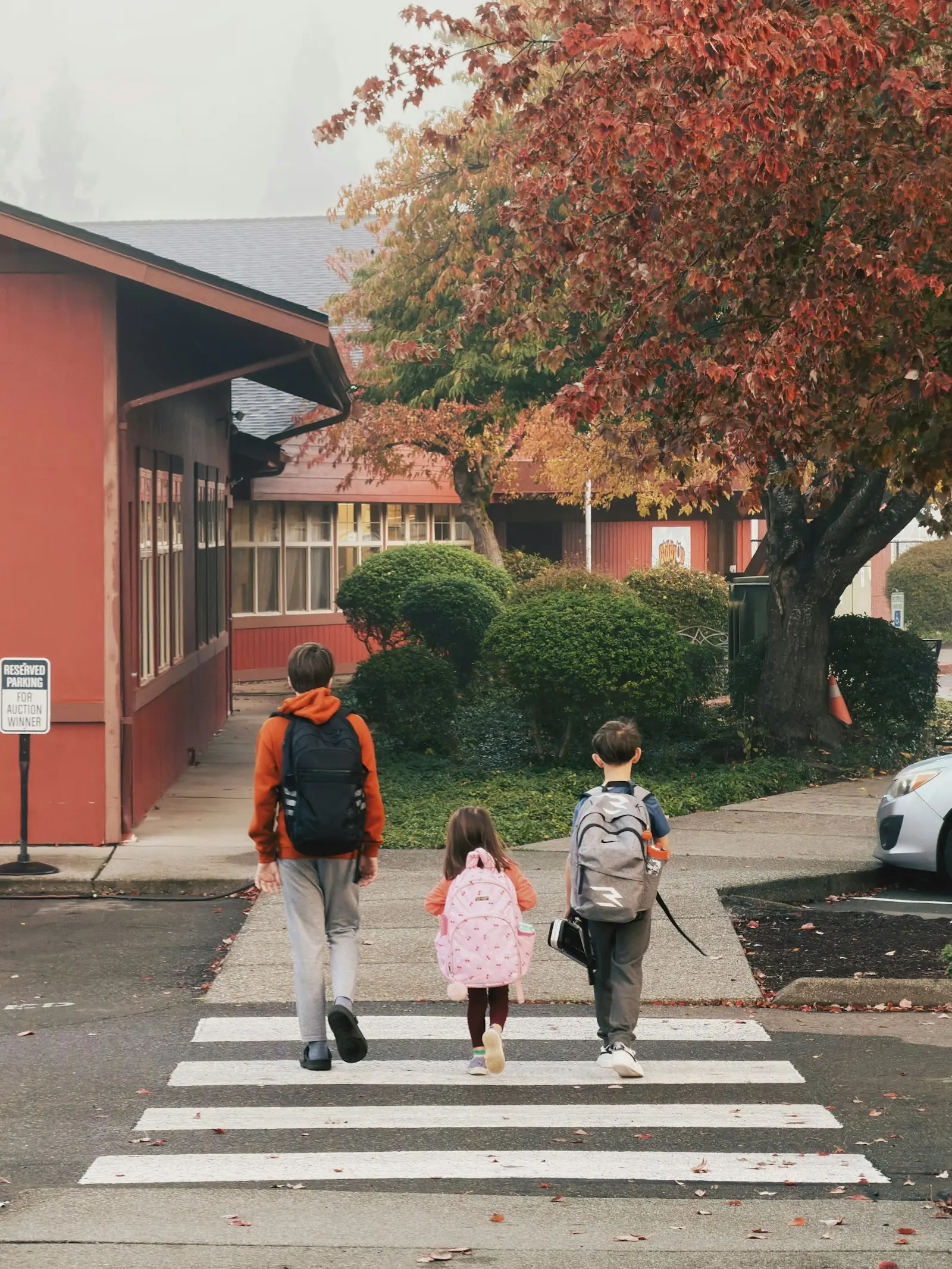Drei Kinder mit Schulranzen auf dem Gehweg, von hinten